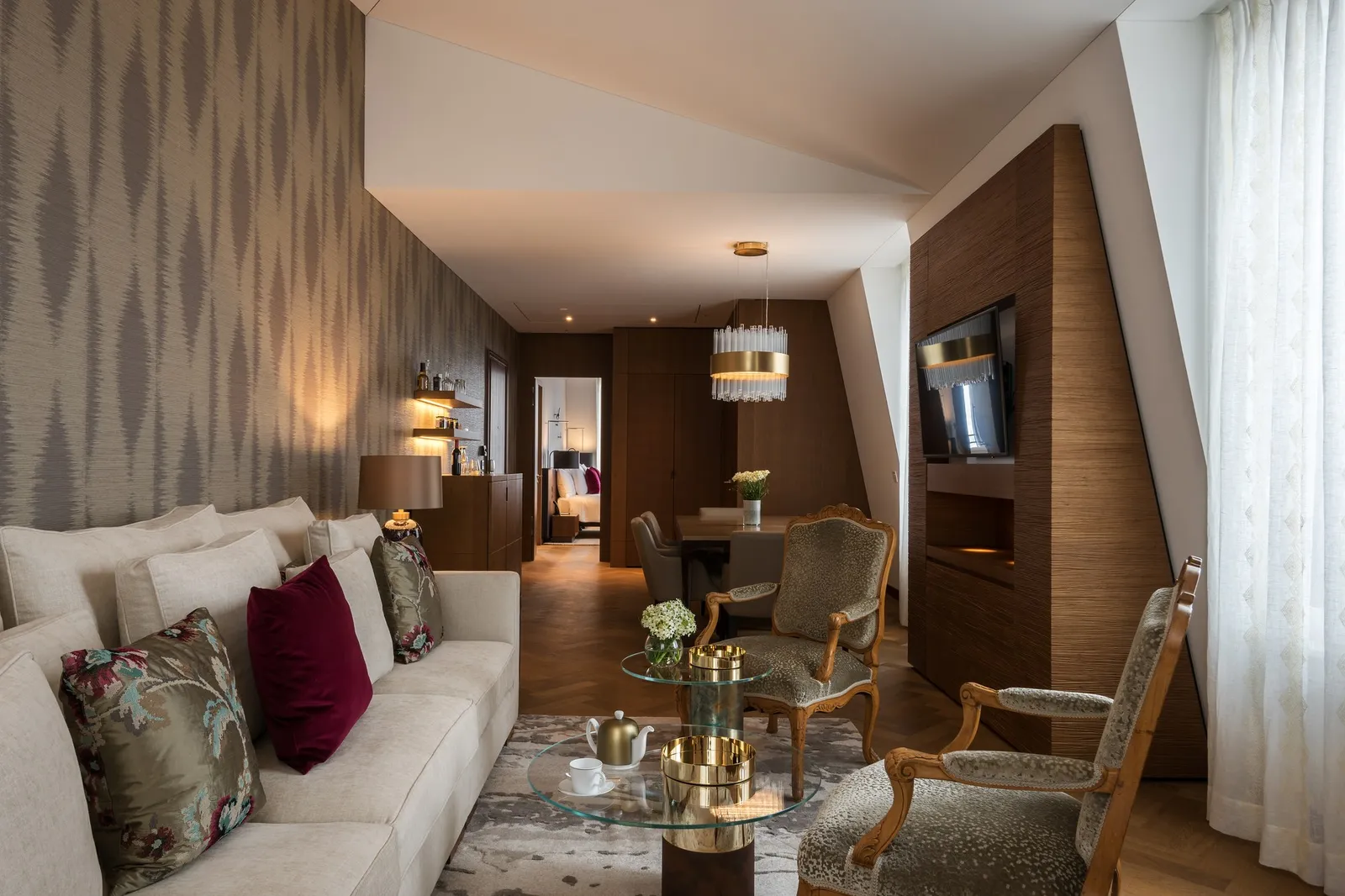 A Heritage Lake View Prestige Suite under the roof: a long sofa with patterned cushions, gilt armchairs, a glass table and a long room behind