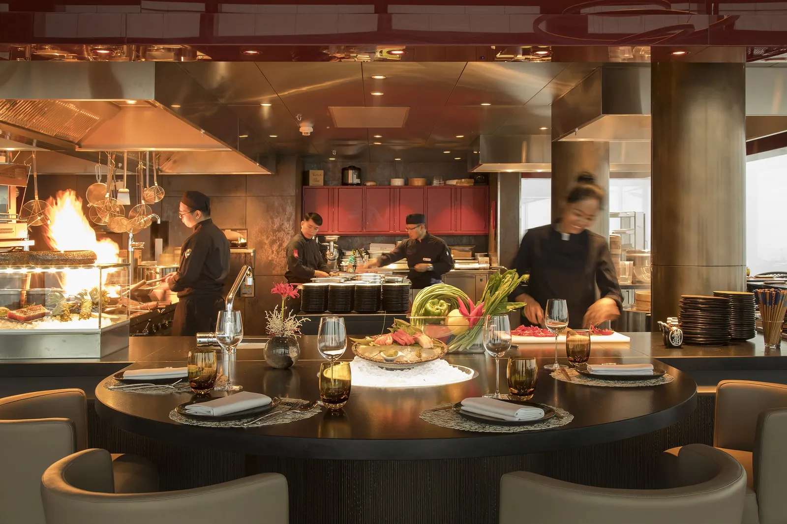 The open kitchen at Spices: chefs at the stations and a wood fire behind a round counter laid for dinner