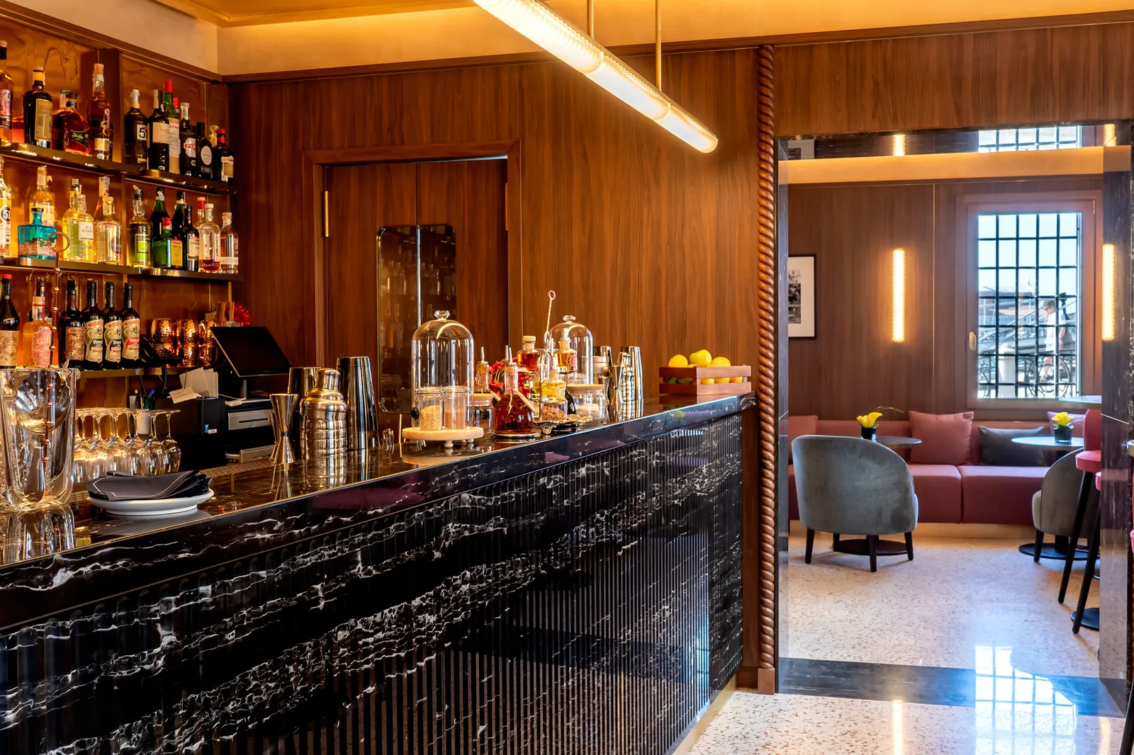 The Alchemia bar counter, with bottles on the shelves and low armchairs