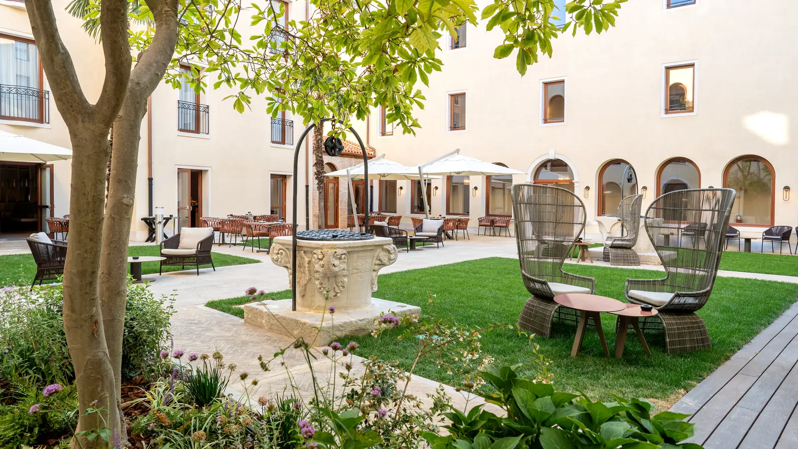 The inner courtyard with its stone wellhead, the lawn, the trees and the wicker armchairs