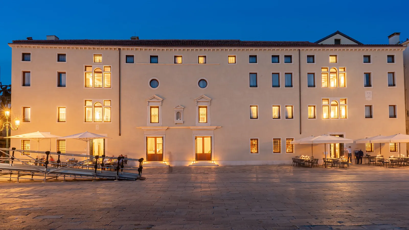 Ca’ di Dio’s waterfront facade at dusk, windows lit and tables under the parasols
