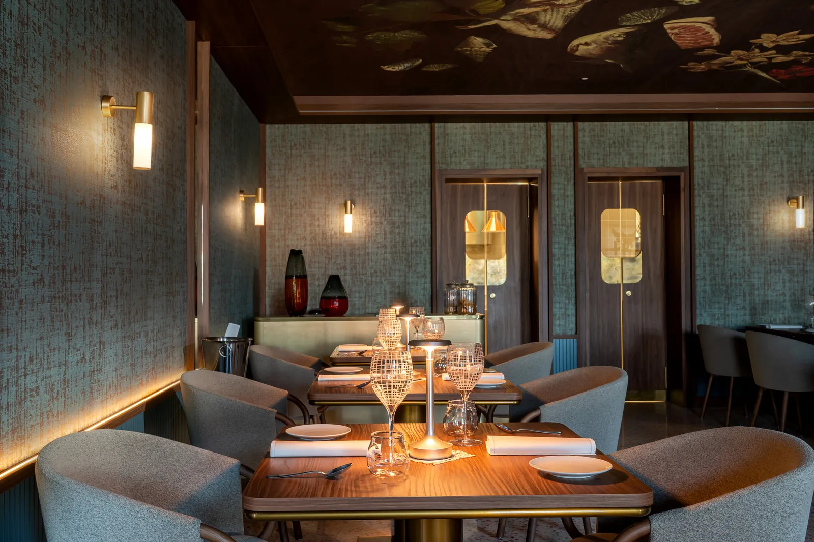 A dining room with a painted ceiling, green fabric walls and laid tables