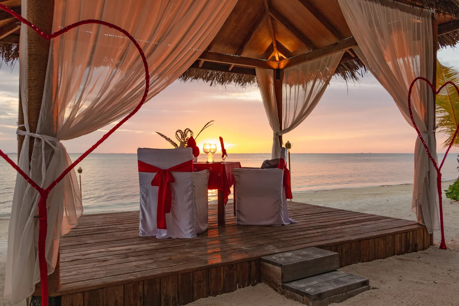 A table for 2 beneath a curtained beach pavilion at sunset