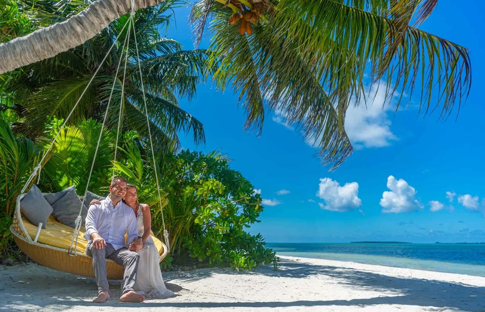 A couple on a swing hung among the palms above the beach