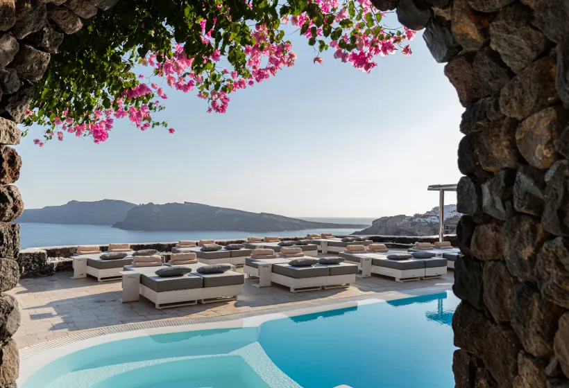 The main pool seen through an arch of lava stone, with bougainvillea in flower, loungers on the terrace and the caldera.