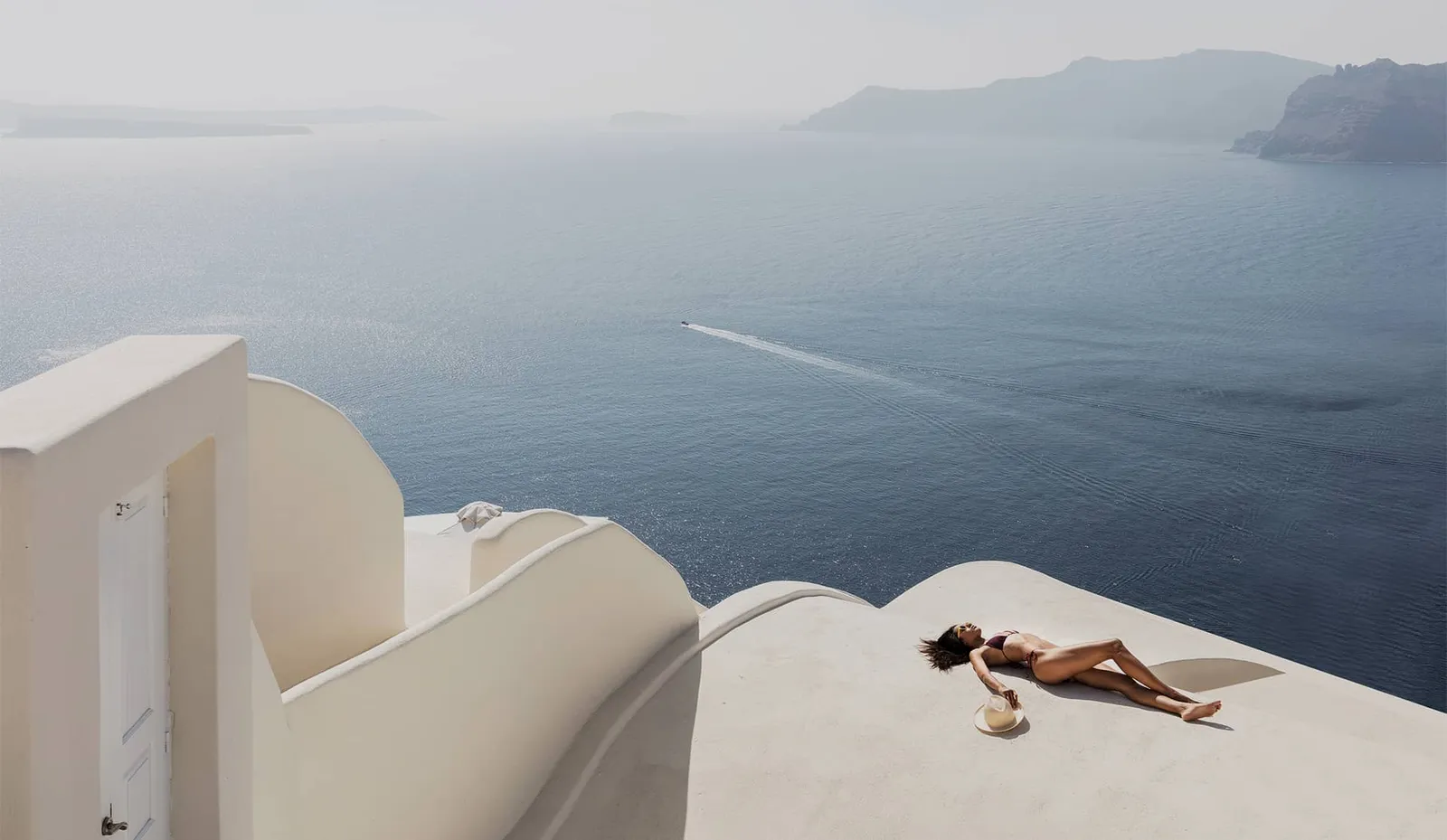 A guest sunbathing on a white vaulted roof above the caldera.