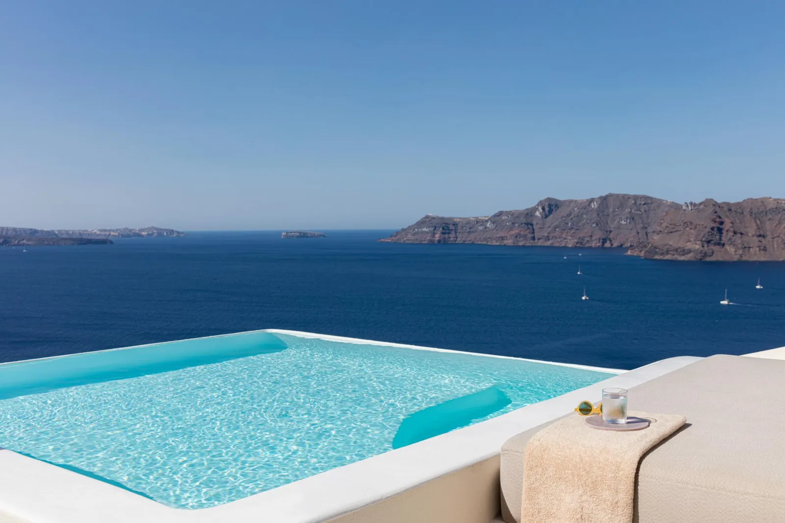 An Infinity Pool Suite’s infinity pool, turquoise above the blue of the caldera, with the cliffs beyond.