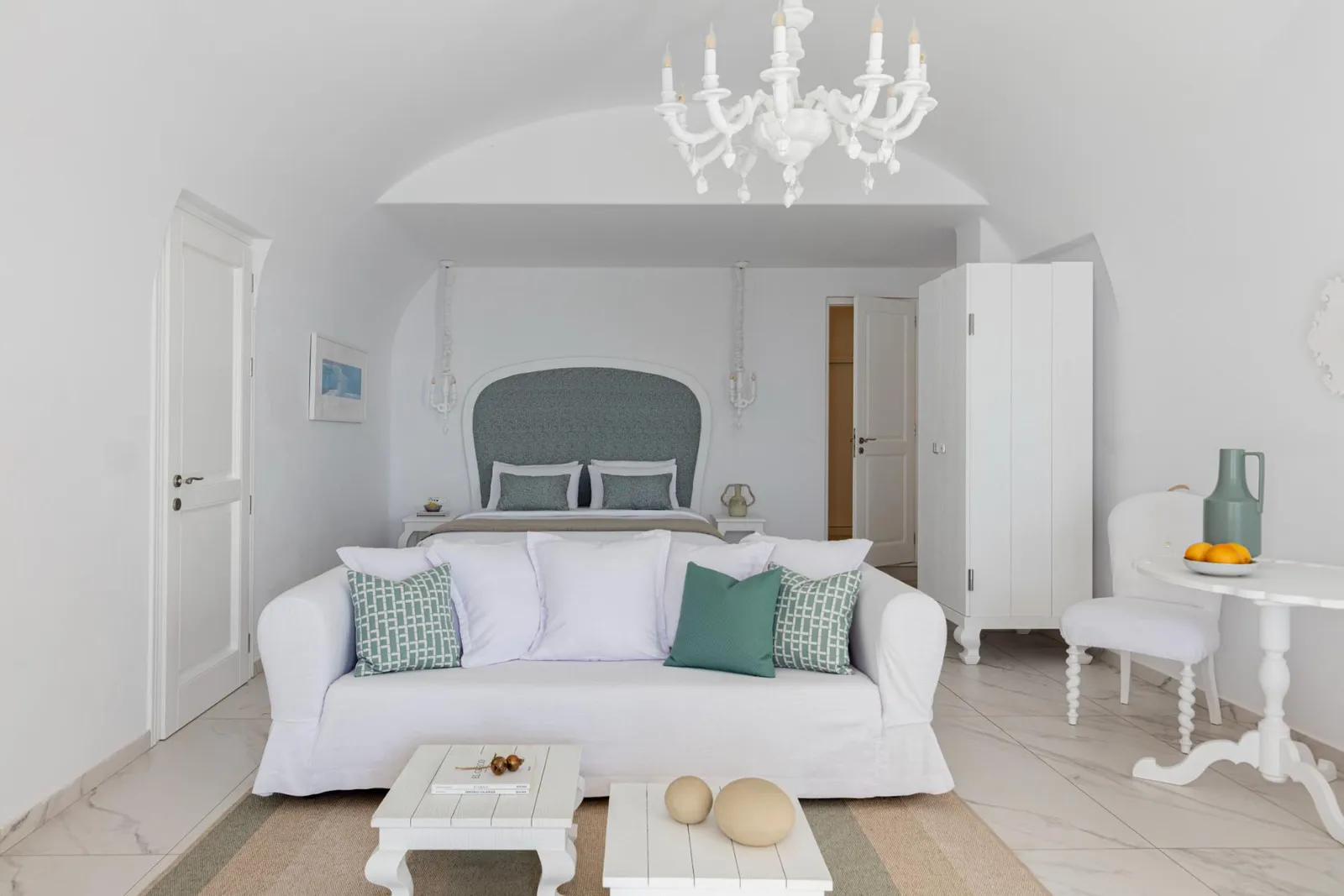 A Pool Suite’s living area: a white sofa with green cushions, a white chandelier under the vault and the bed behind.