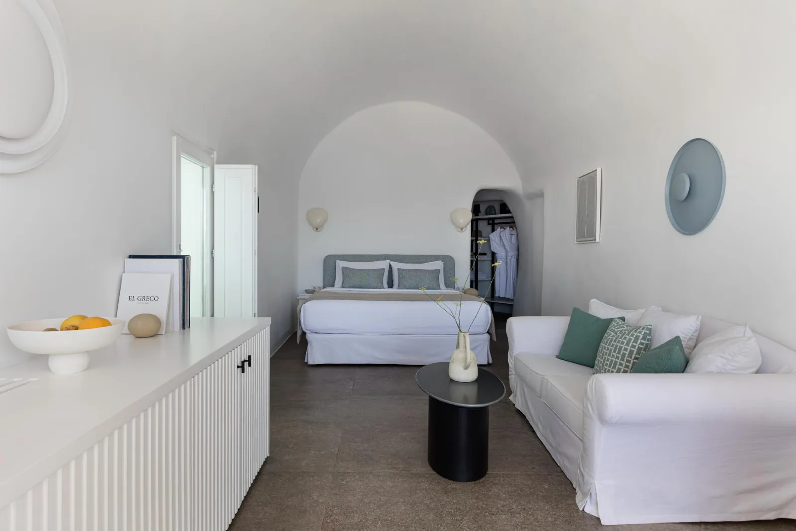 Inside a River Pool Suite: the bed in an arched alcove, a white sofa, a black side table and whitewashed walls.