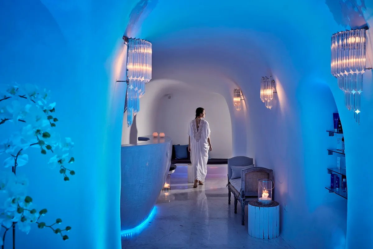 The spa cut into the rock, lit in blue: a figure in a white robe among the vaults, the armchairs and the crystal lamps.