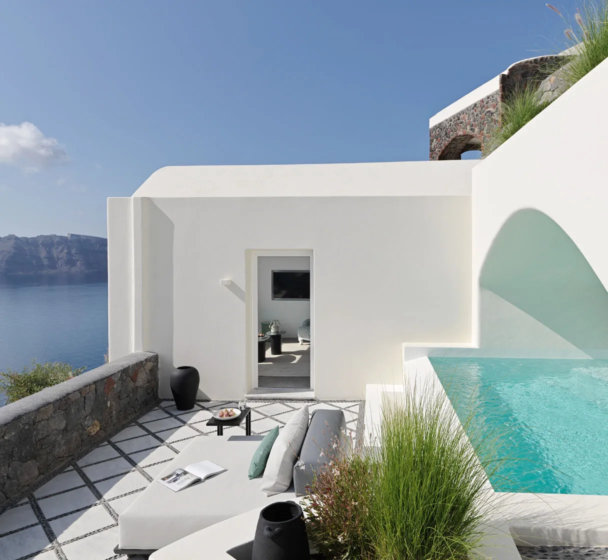 A white villa with a sea-green arched niche, the pool, loungers on a diamond-patterned floor and a stone wall.