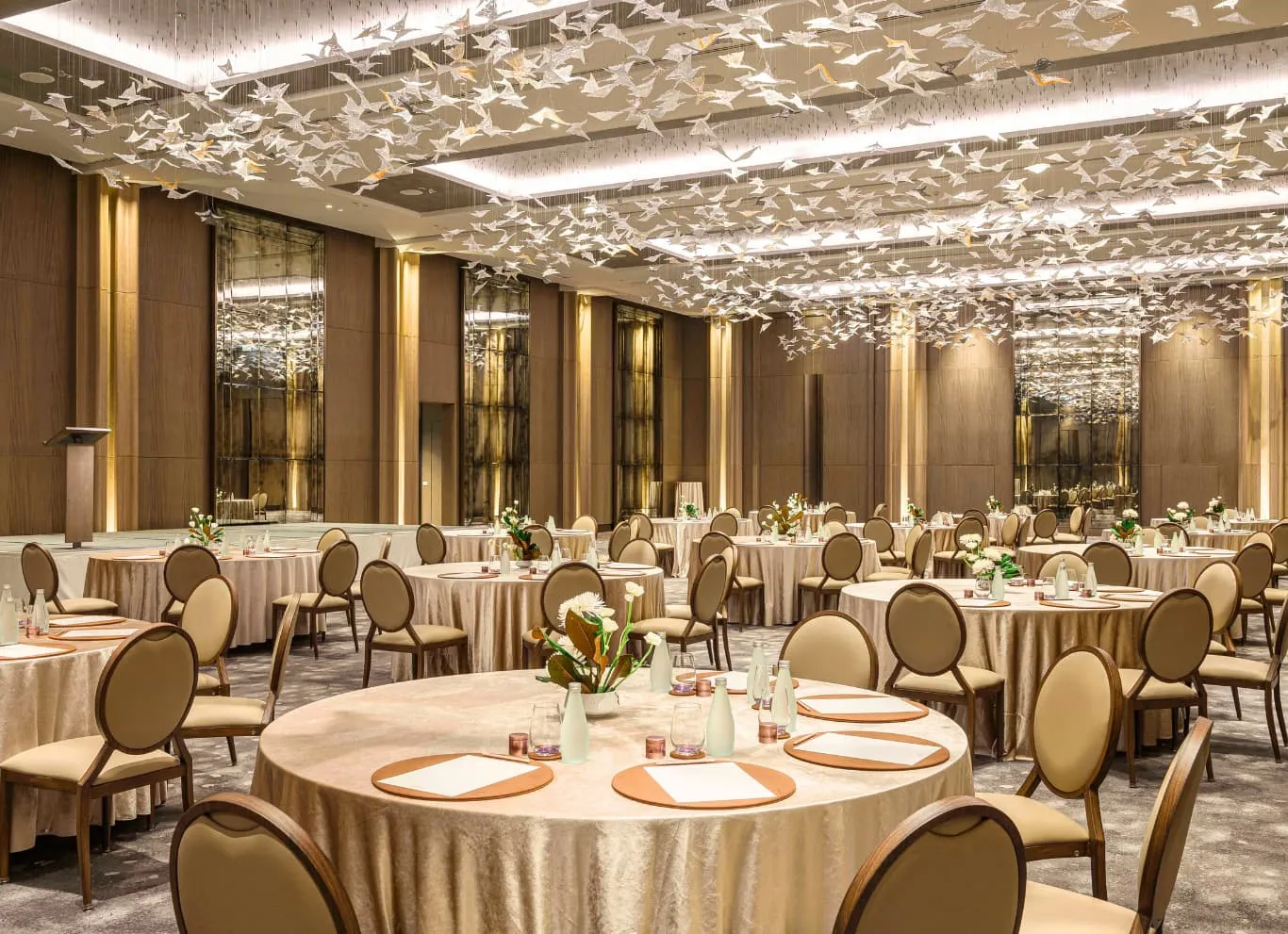 La Ballroom apparecchiata per una cena: tavoli rotondi, un soffitto di lampade a foglia e le finestre sul fiume.