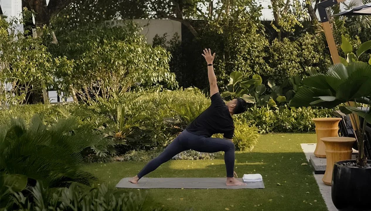 Yoga sul prato del giardino di una villa, fra siepi e alberi, la mattina.
