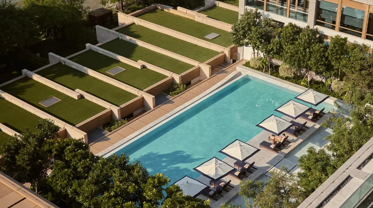 La piscina a sfioro vista dall’alto: lettini e ombrelloni bianchi su un lato, prati a gradoni e gli alberi del giardino tutto intorno.