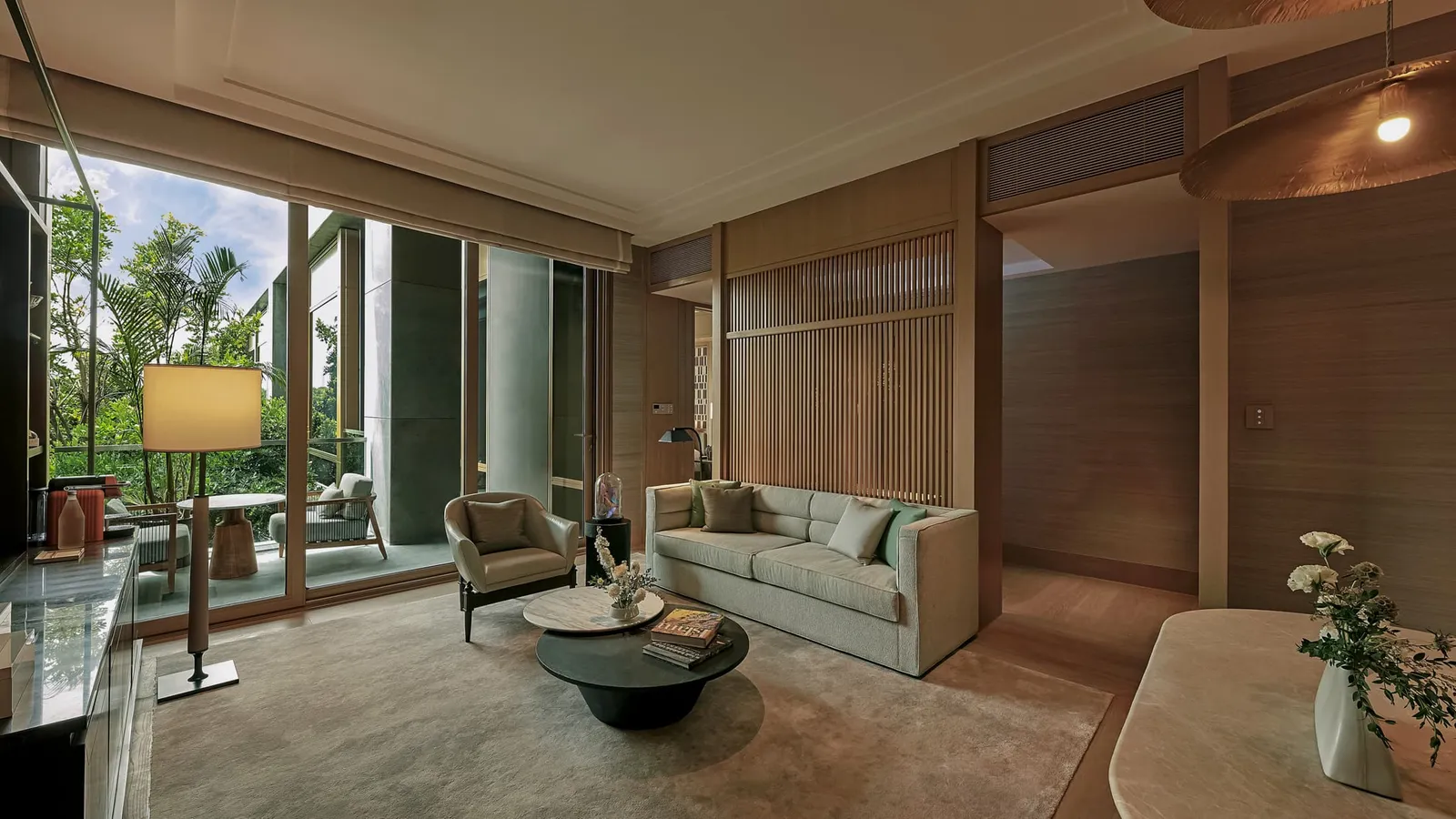 Il soggiorno di una Courtyard Suite: divano, tavolino rotondo e la porta a vetri sul balcone e sugli alberi.