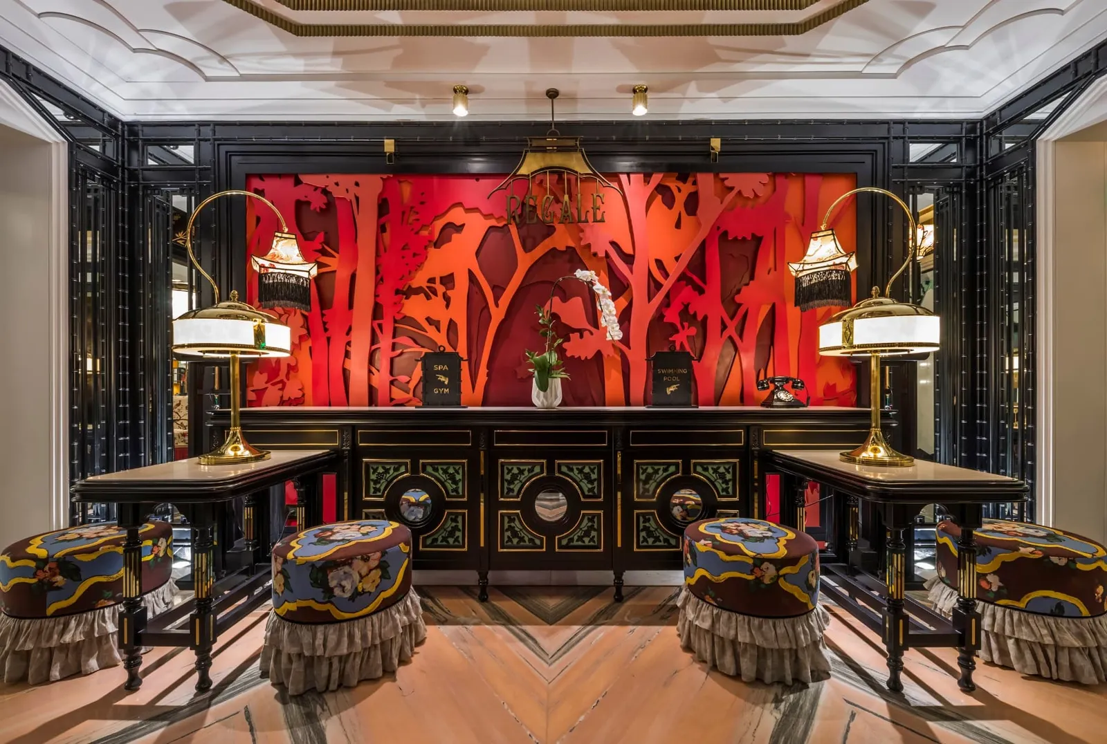 A red lacquered wall with golden trees, 2 desks with lamps and embroidered stools