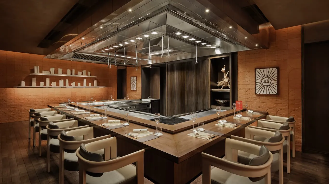 The teppanyaki counter at Hibana by Koki, its hood above the steel grill, leather chairs around it