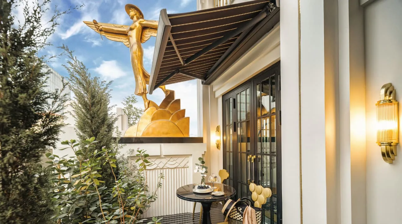 A terrace with a gilded winged statue, a striped awning and a breakfast table
