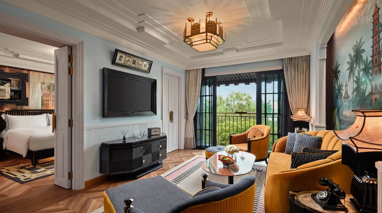 A Deluxe Suite: sitting room with a yellow sofa and a palm-tree mural, the bed next door