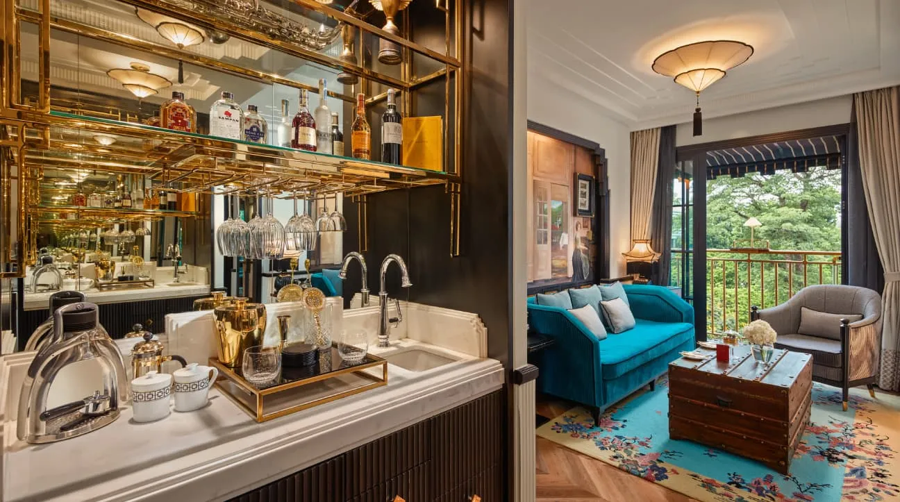 The Junior Suite’s bar with glasses and bottles, a blue sofa and a green balcony