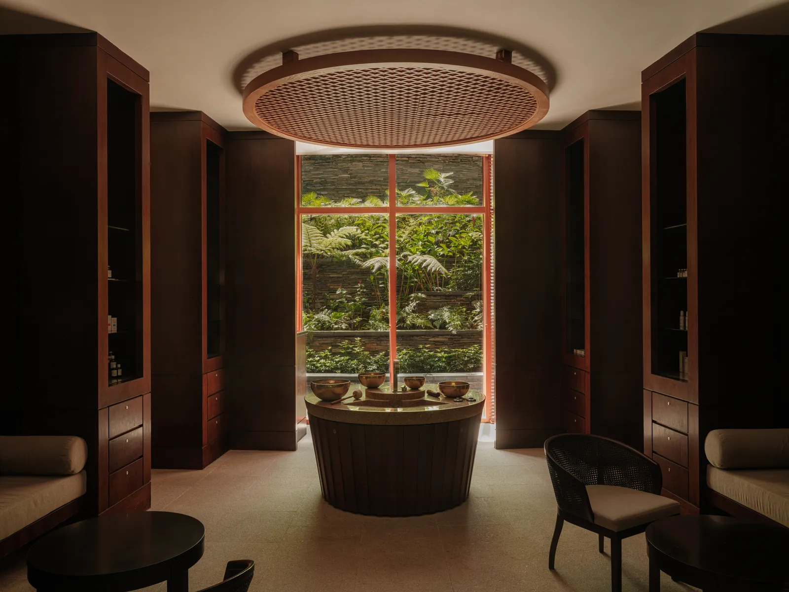 Auriga Spa: a round basin under a circular lattice ceiling, dark timber cabinets on either side and a tall window on a wall of ferns.