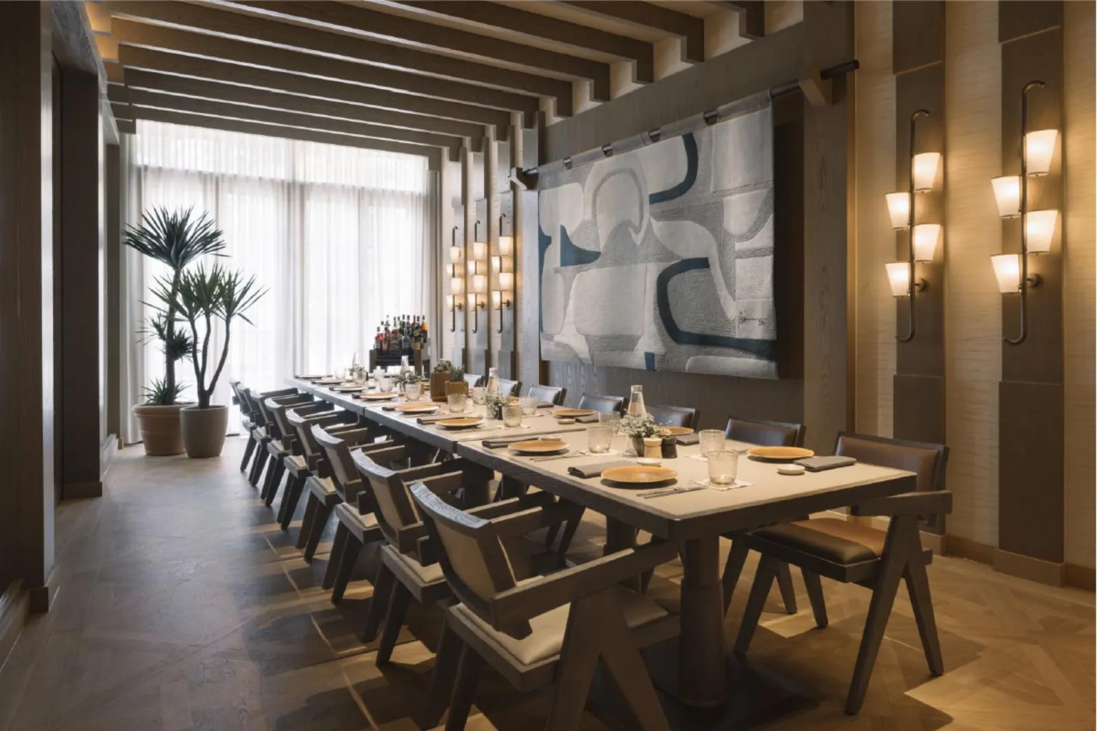 Fiamma’s private dining room: a long table set for dinner under timber beams, wall lamps and a pale mural.