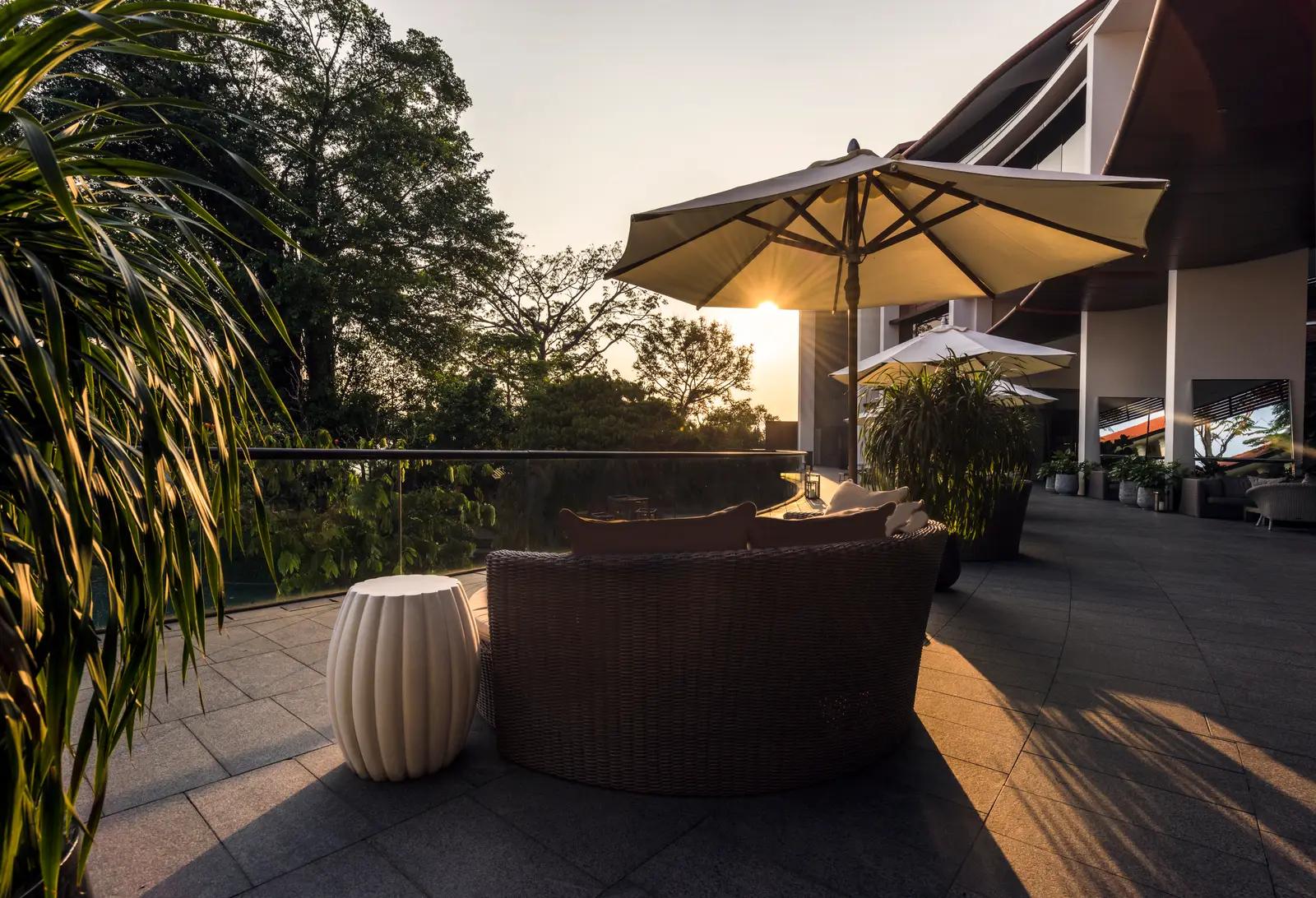Bob’s Bar’s terrace at sunset: a wicker sofa under a parasol, the glass balustrade over the treetops and, on the right, the hotel’s curved wing.