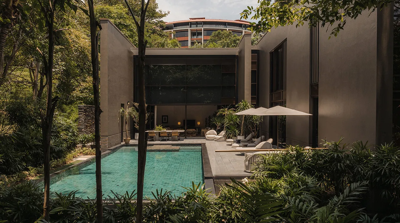 The Capella Manor’s pool: a long green pool between dark walls and trees, sunbeds and a parasol at the far end, the hotel’s curved roof above.