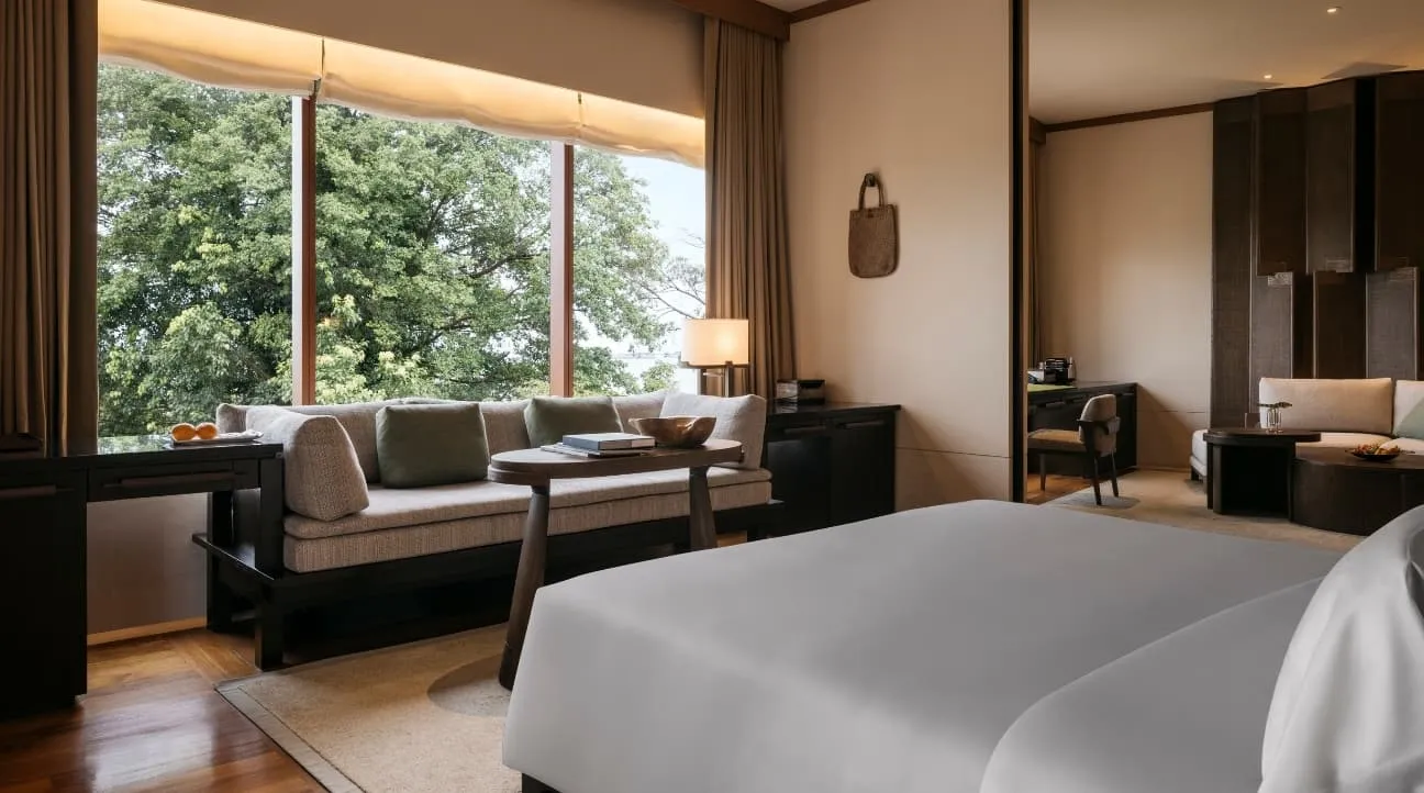 A Capella Suite’s bedroom: the bed, a long sofa under windows full of trees and a timber floor.