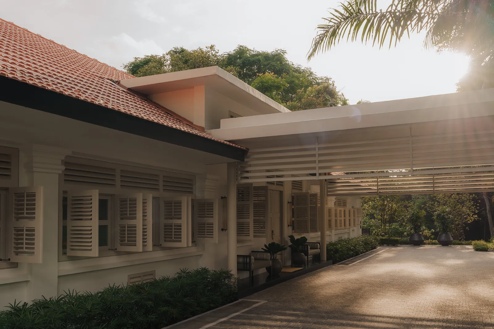 A Colonial Manor: the white bungalow with louvred shutters and a red-tiled roof, a covered walkway and the paved court in evening light.