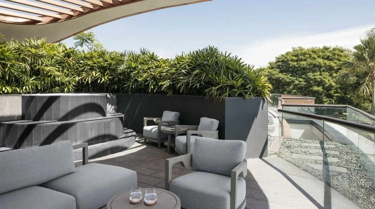 A Constellation Room’s terrace: grey armchairs round a low table, the stone steps of the Jacuzzi on the left, planting and treetops behind.