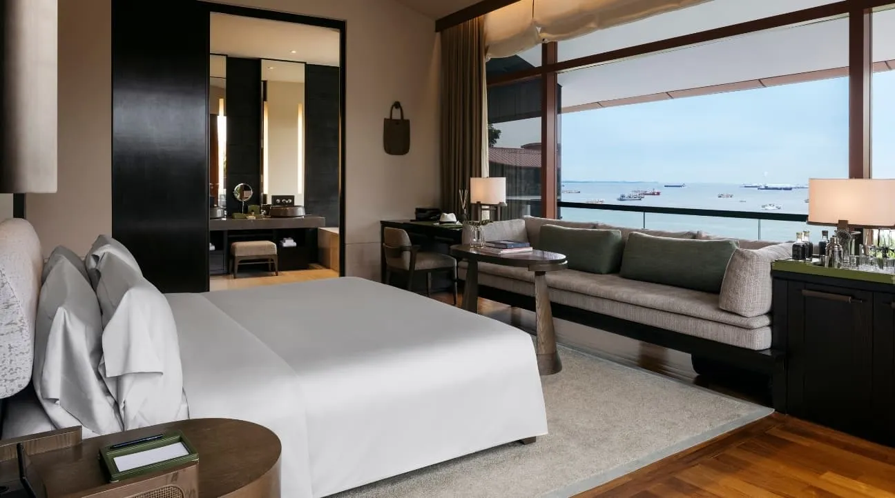 A Premier Seaview Room: the bed, a daybed under the windows and the sea with ships at anchor beyond the balcony.