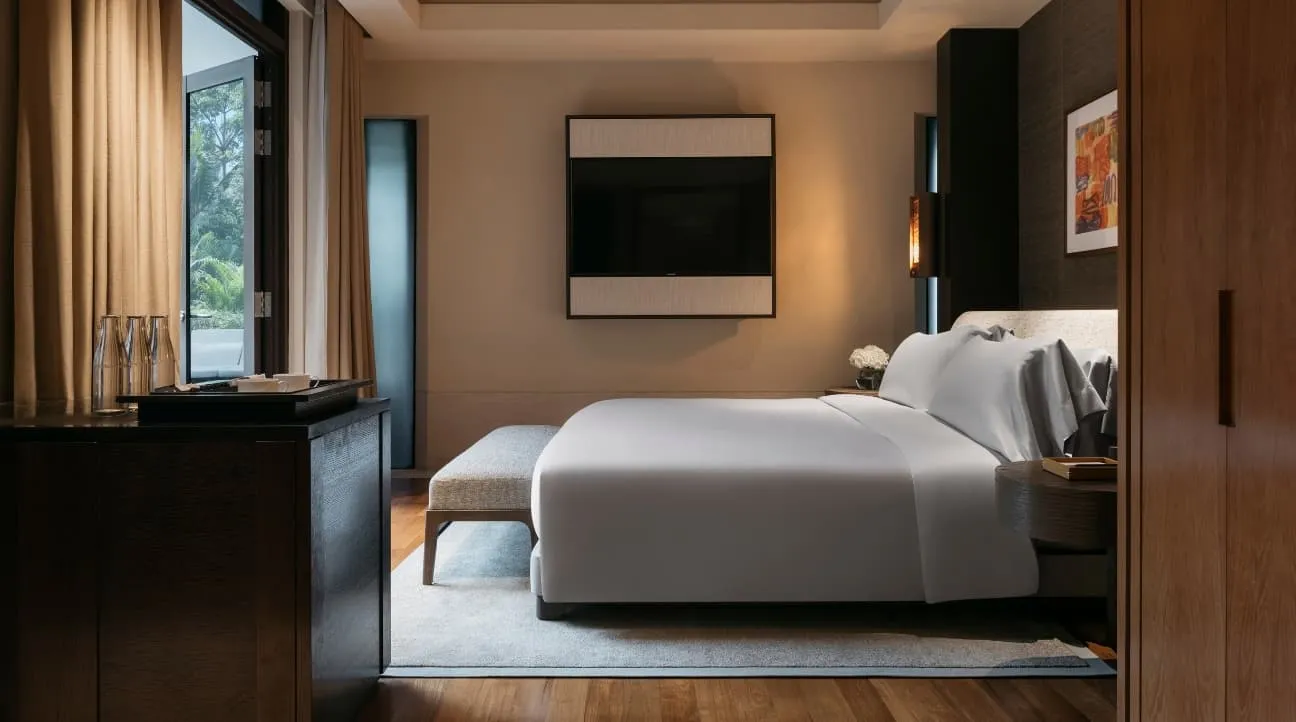 A bedroom of a Two-Bedroom Villa: the bed with a bench at its foot, a television on the far wall and a window on the garden to the left.