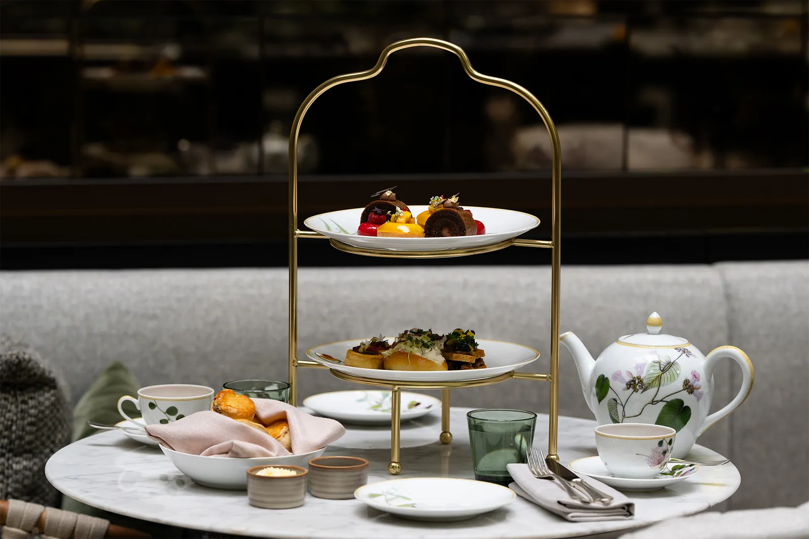 Afternoon tea at Aperture: a gilded 2-tier stand of pastries, a floral teapot and cups on a marble table