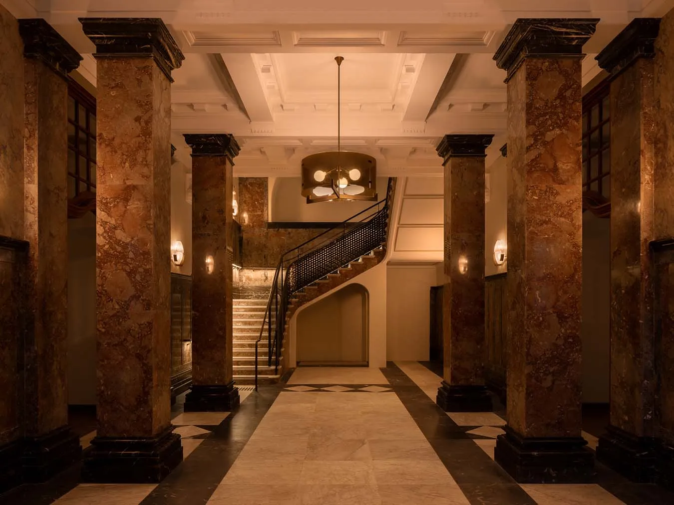 The entrance hall of the old Department of Education: marble columns, a pendant lamp and a curving staircase
