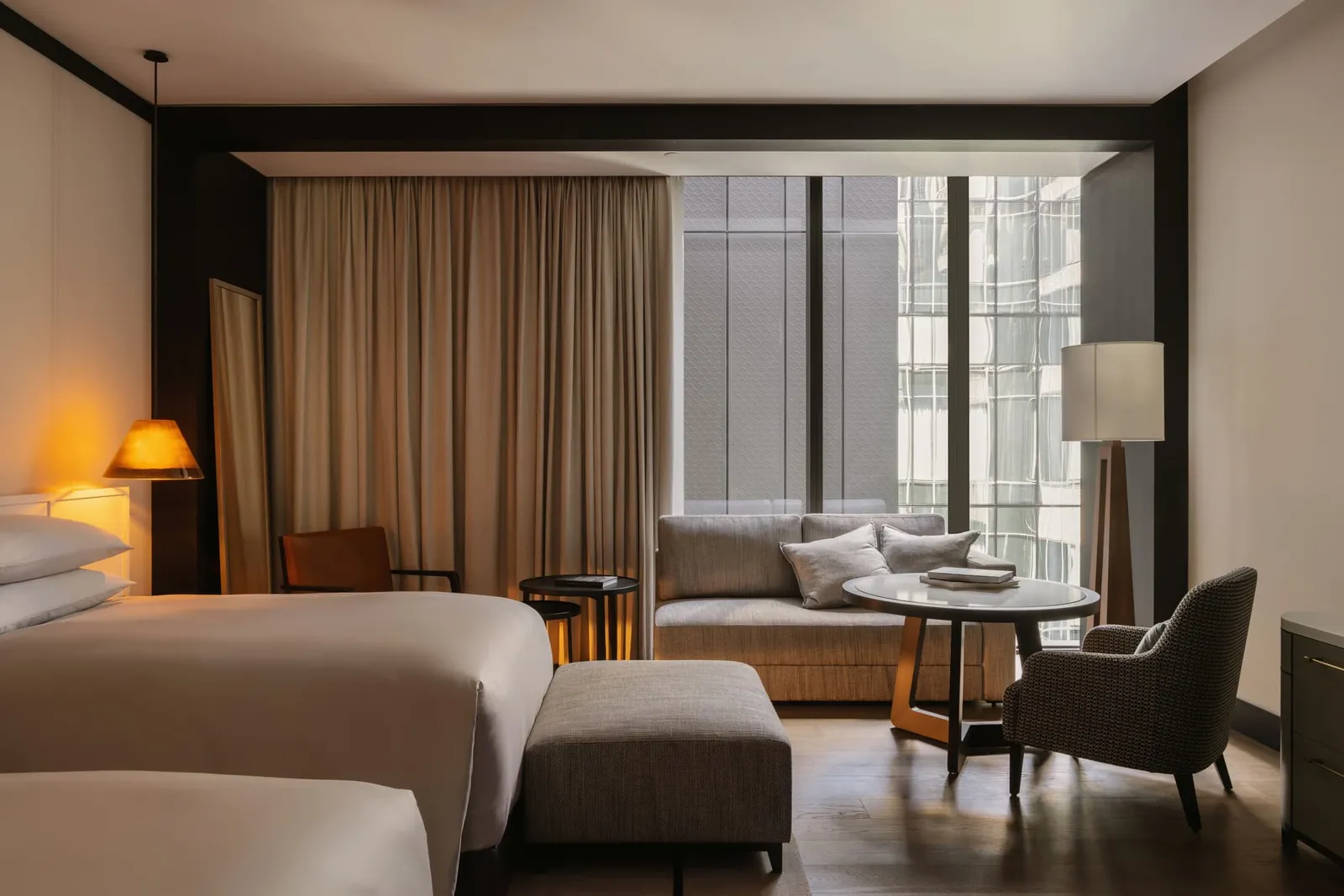 A Deluxe Room: a king bed, a sofa and a round table in front of tall windows