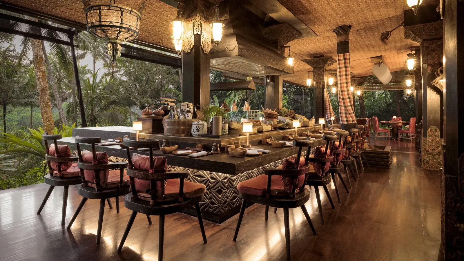 Api Jiwa in the evening: the long chefs’ counter with its padded chairs, the lanterns lit and the forest beyond the open tent.