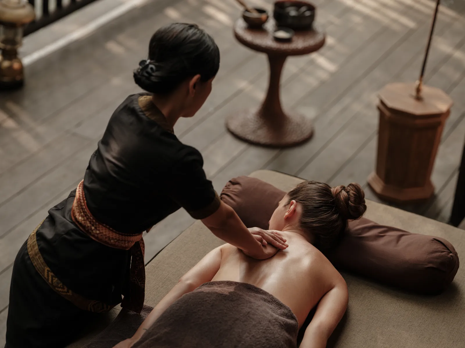 A massage at Auriga: the therapist in black presses on the back of a guest lying on the couch, on a wooden floor.