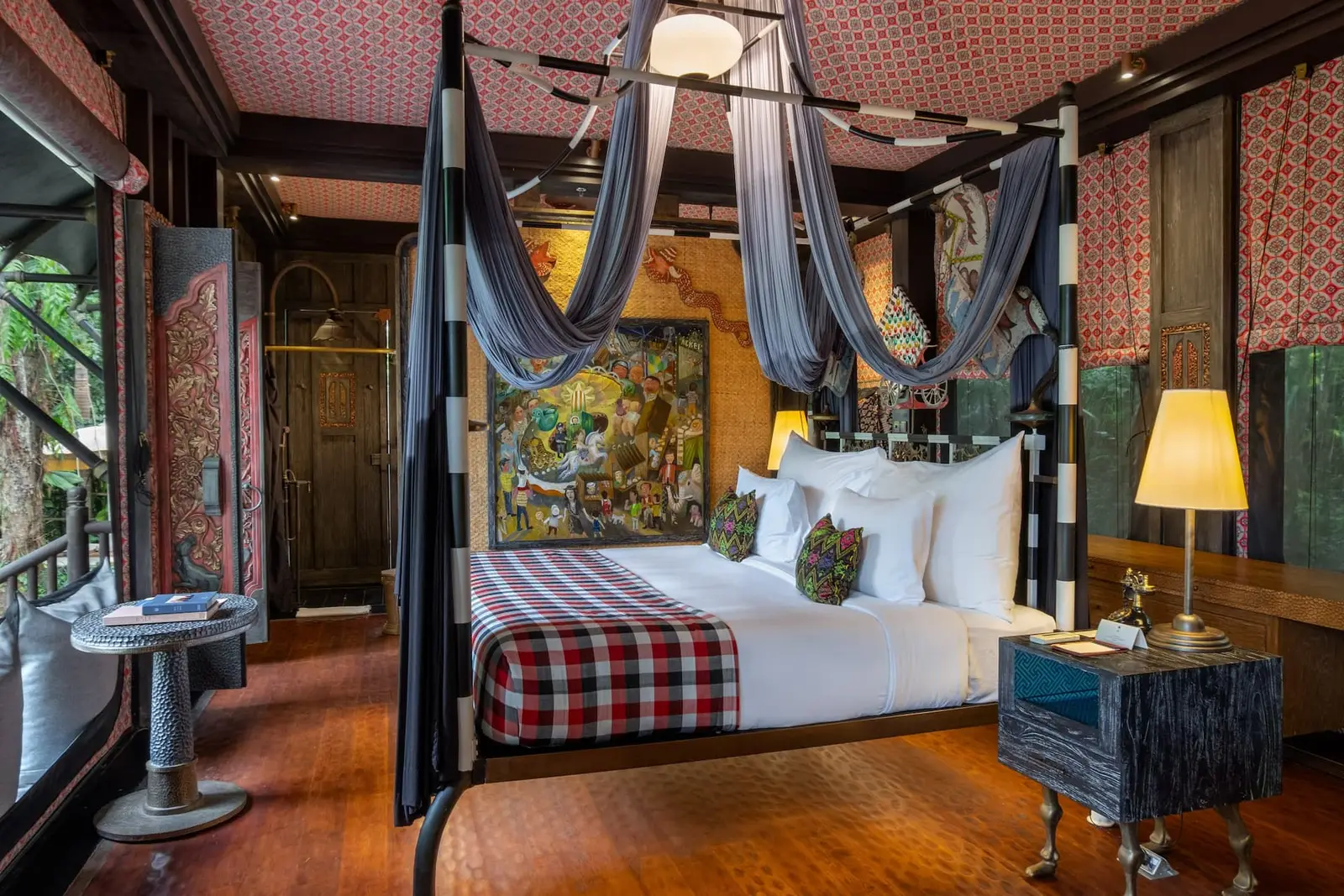A Forest Tent’s bedroom: the check-covered bed under grey drapes, a large Balinese painting behind it and a lamp alight.