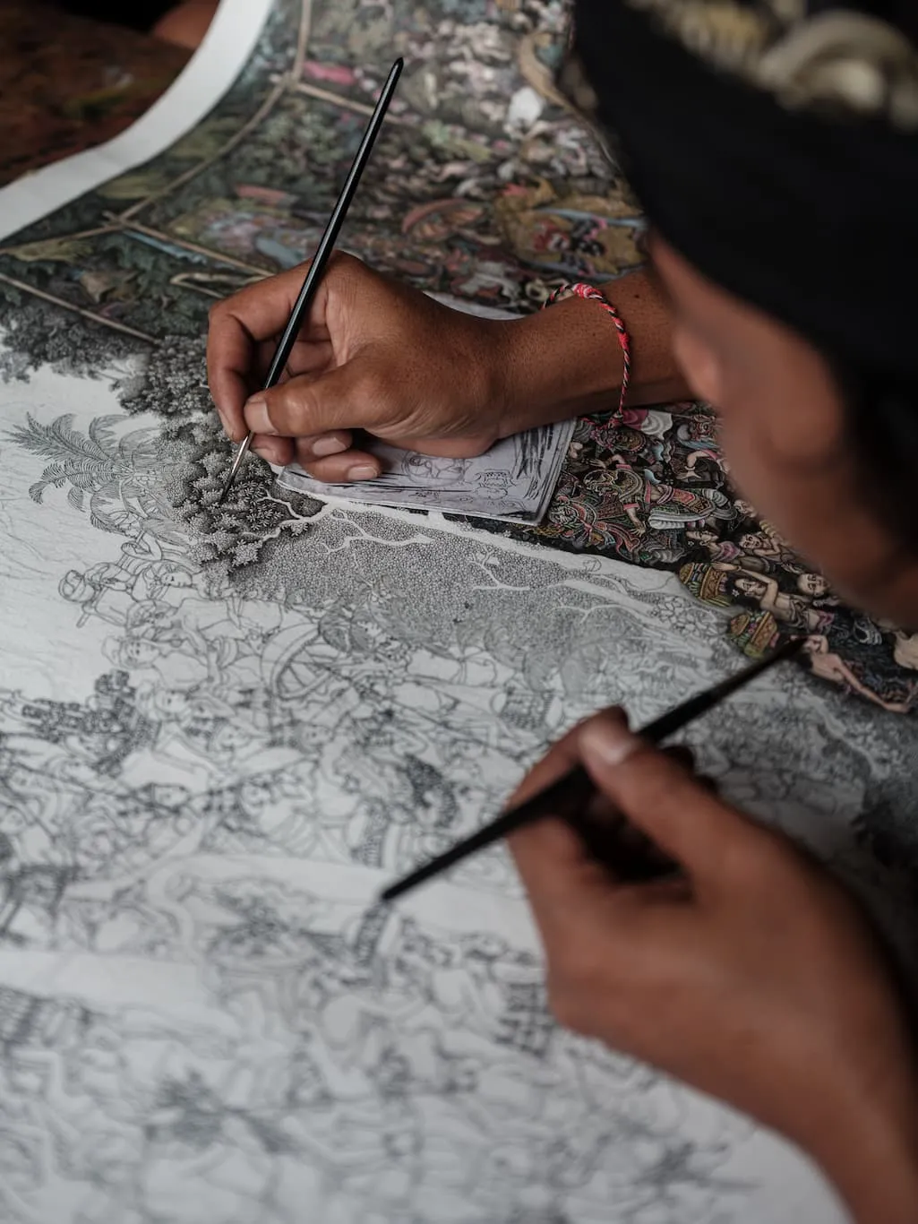 A hand painting with a fine nib on a canvas in the Keliki style, dense with black-and-white figures.