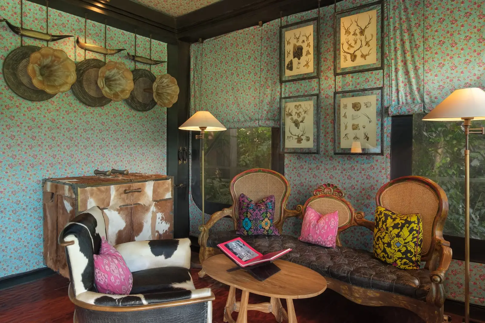 The sitting corner of a Keliki Tent: a cowhide armchair, a carved wooden sofa, hats and botanical plates on the walls.