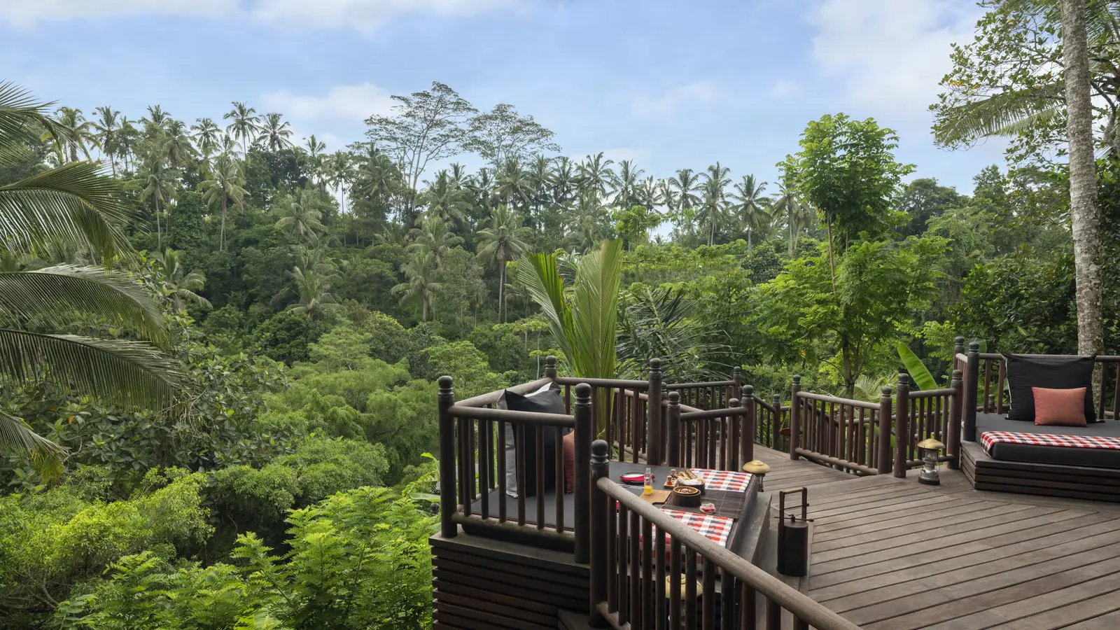 The Two Bedroom Lodge’s deck: a laid table, a daybed and the Keliki valley covered in forest.