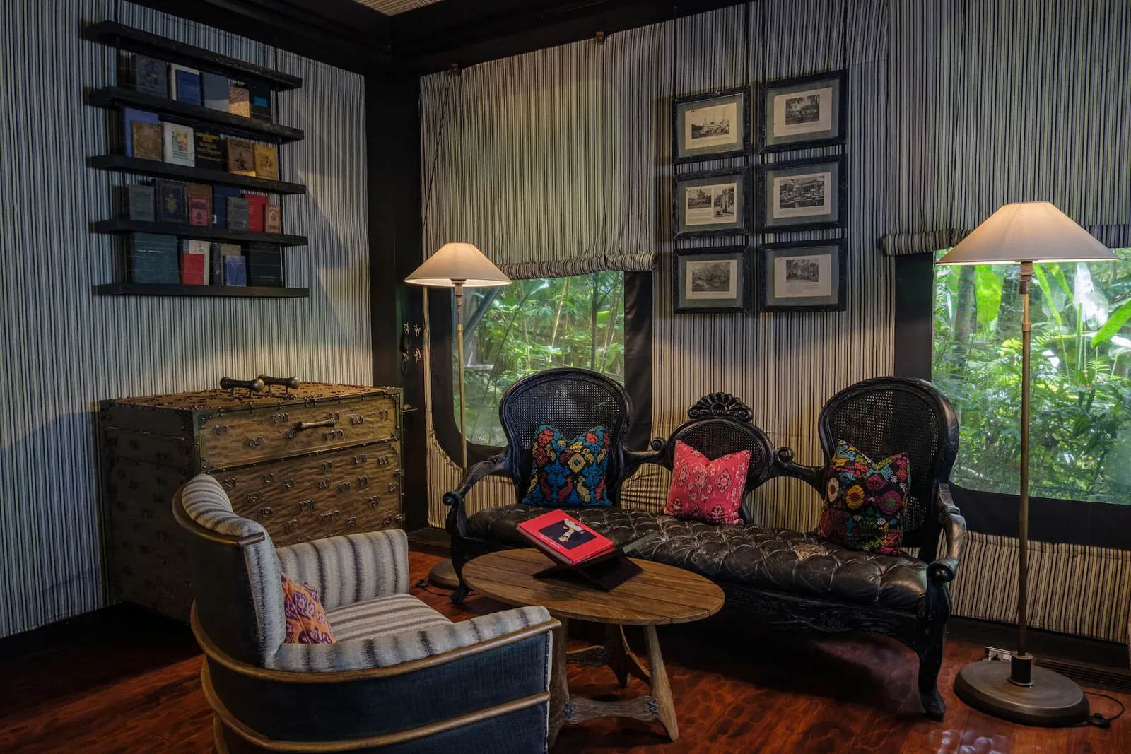 A Terrace Tent’s sitting room: a black wooden sofa, a striped armchair, books on a shelf and the window onto the trees.