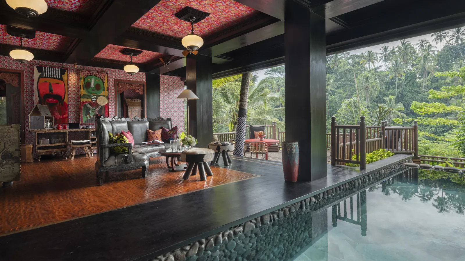 The Two Bedroom Lodge’s living room open onto its heated pool: sofas, painted masks on the walls and the valley beyond the balustrade.