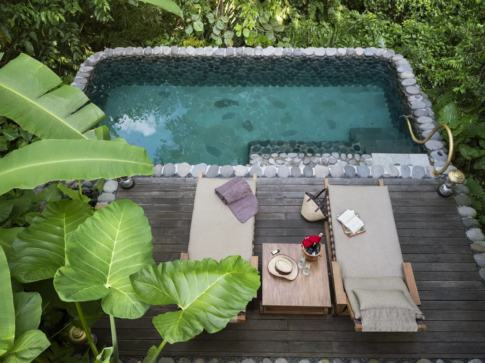 A Valley Tent’s pool from above: 2 loungers on the wooden deck, a small table and large tropical leaves all round.