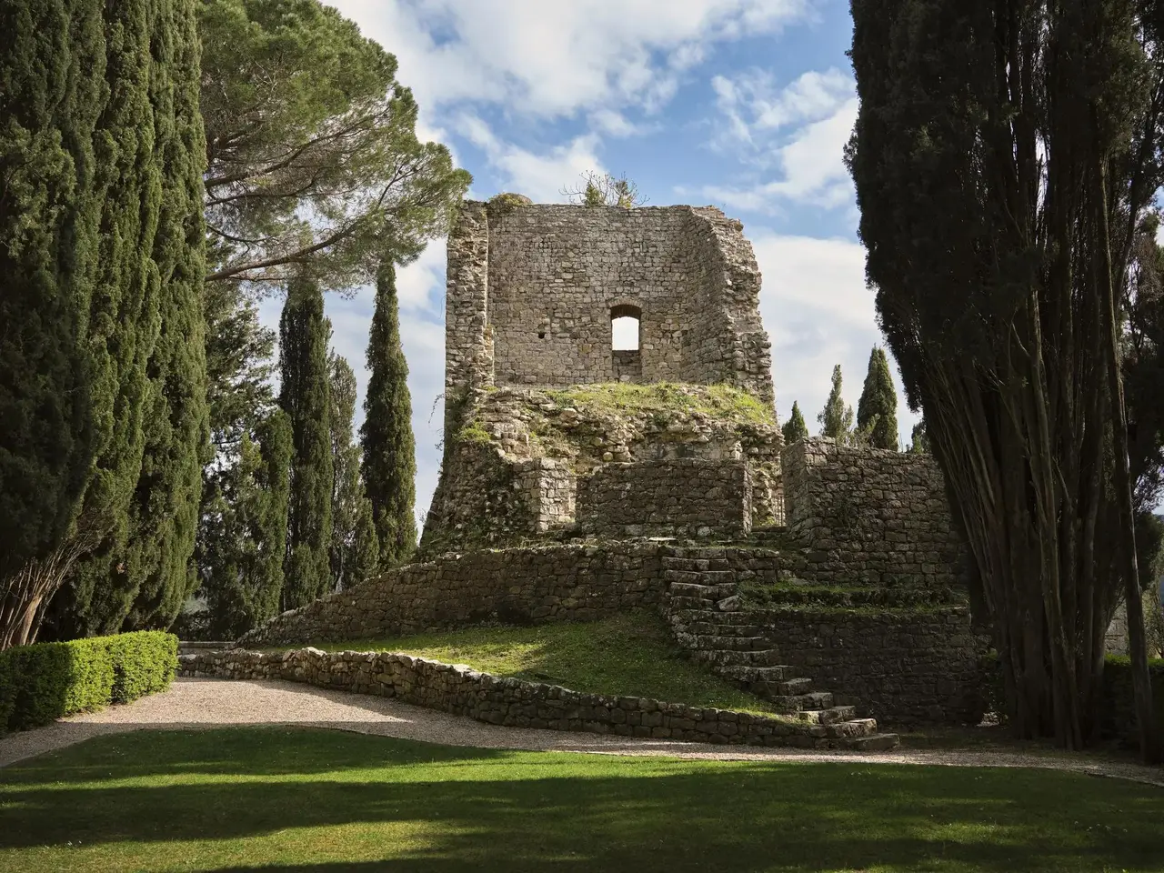 The ruins of the medieval castle among the cypresses, with the lawn and stone steps in front.