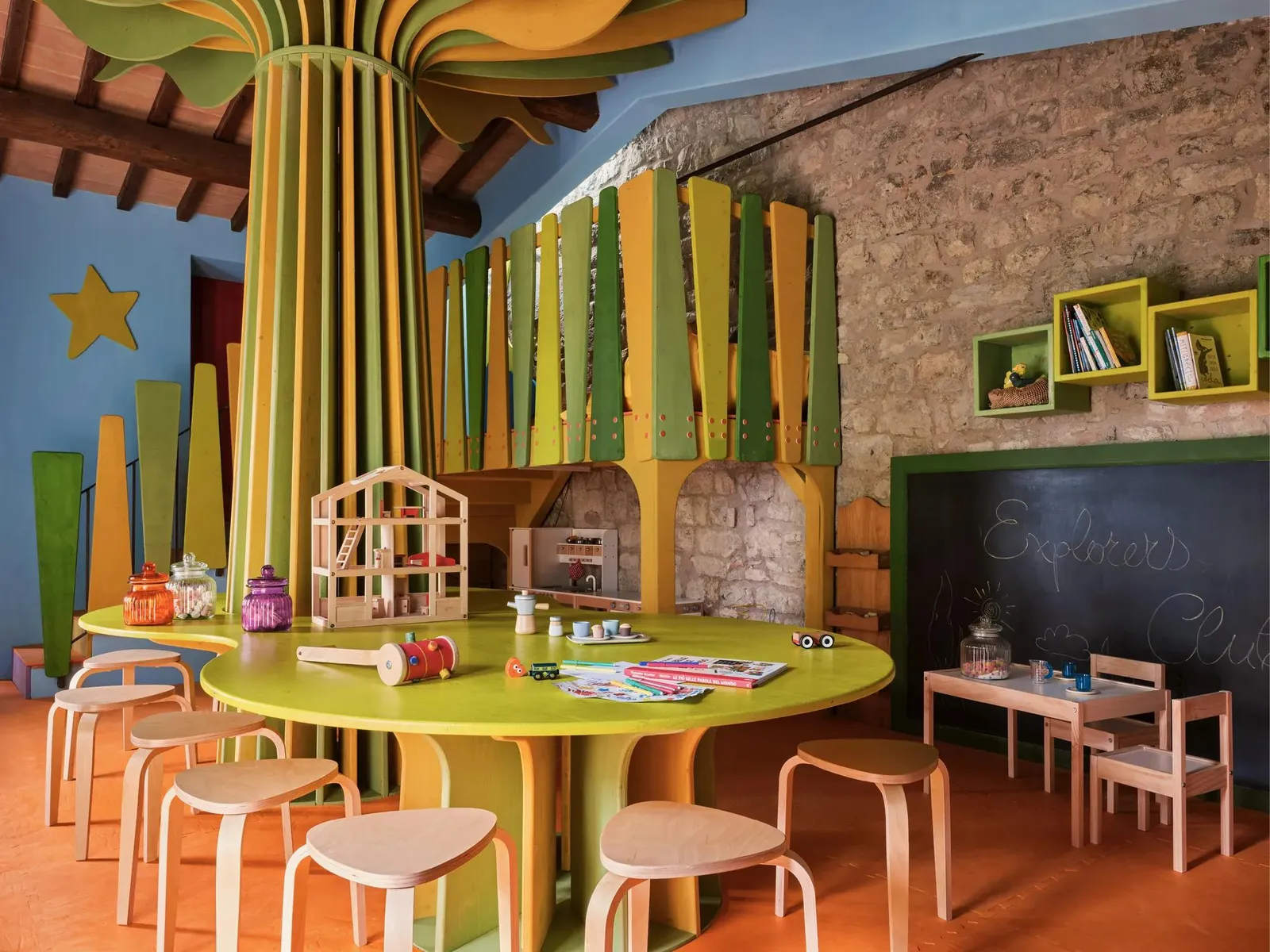 The Kids’ Club, a big painted wooden tree in the middle, low coloured tables and a blackboard on the stone wall.