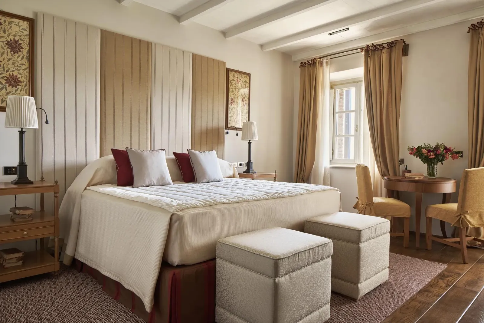 A Junior Suite bedroom: the bed with its striped headboard, 2 footstools at its end and the desk under the window.