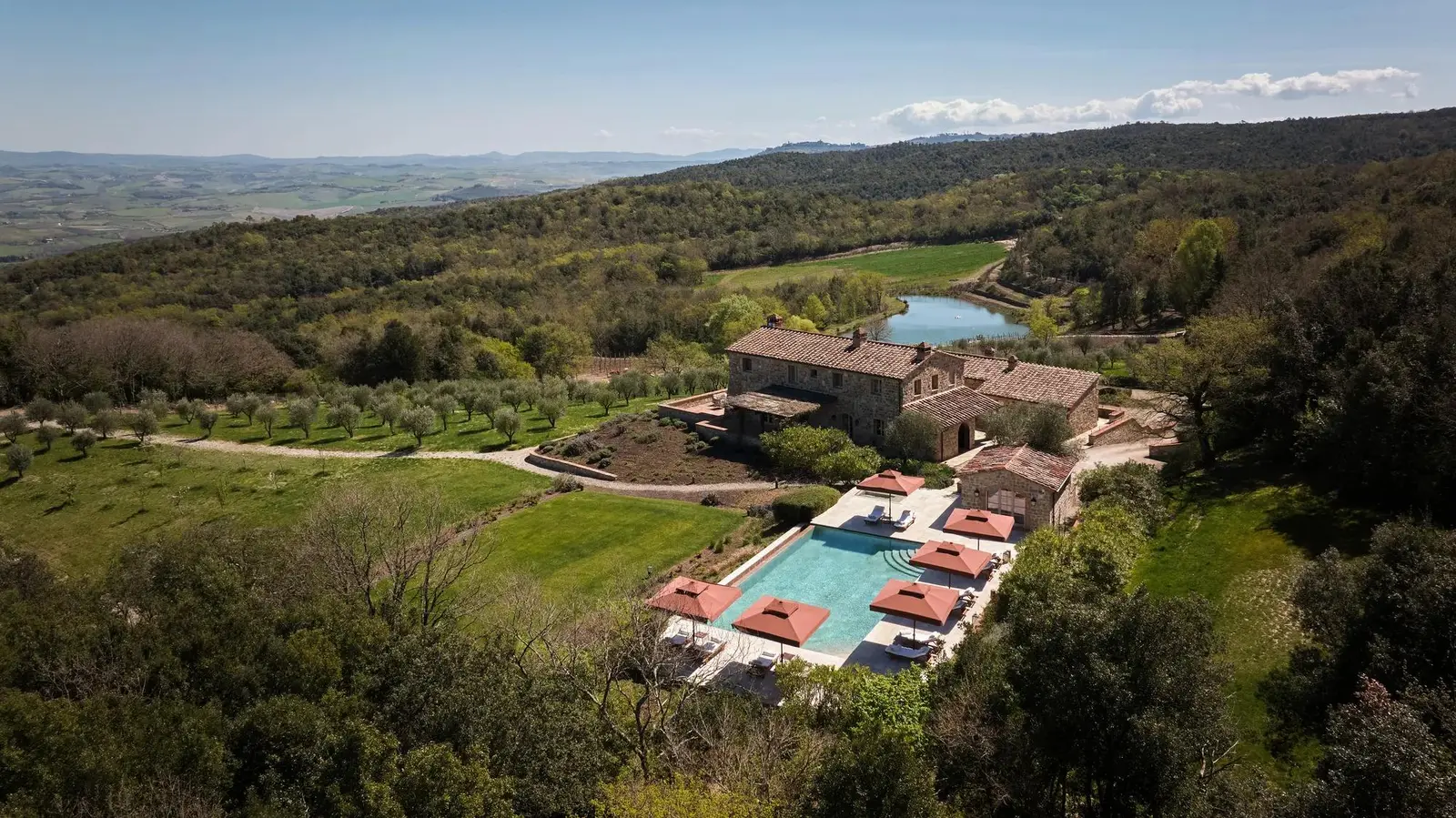 Villa Agresto from above: the house between the woods and the fields, the pool with red parasols and the valley to the horizon.