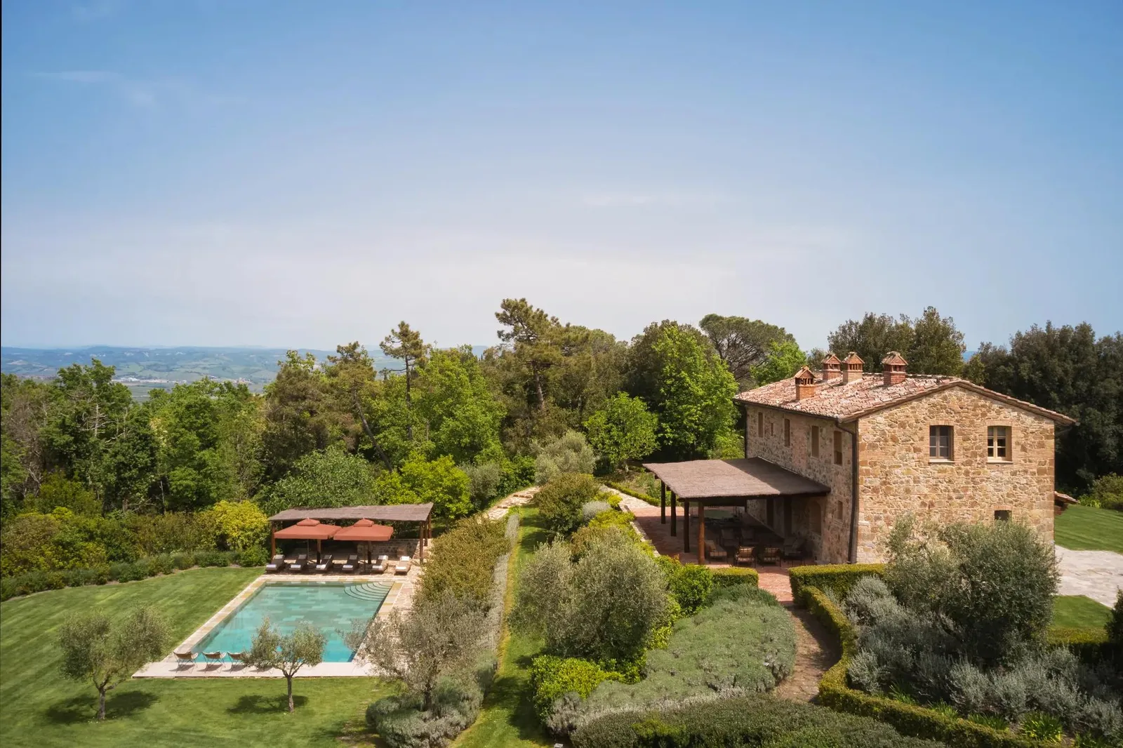 Villa Alba: the stone farmhouse, the pergola and the pool on the lawn, with the valley behind.
